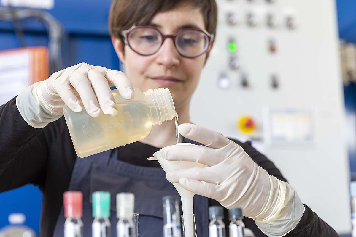Eine Wissenschaftlerin schüttet eine Flüssigkeit in ein Reaktionsgefäß